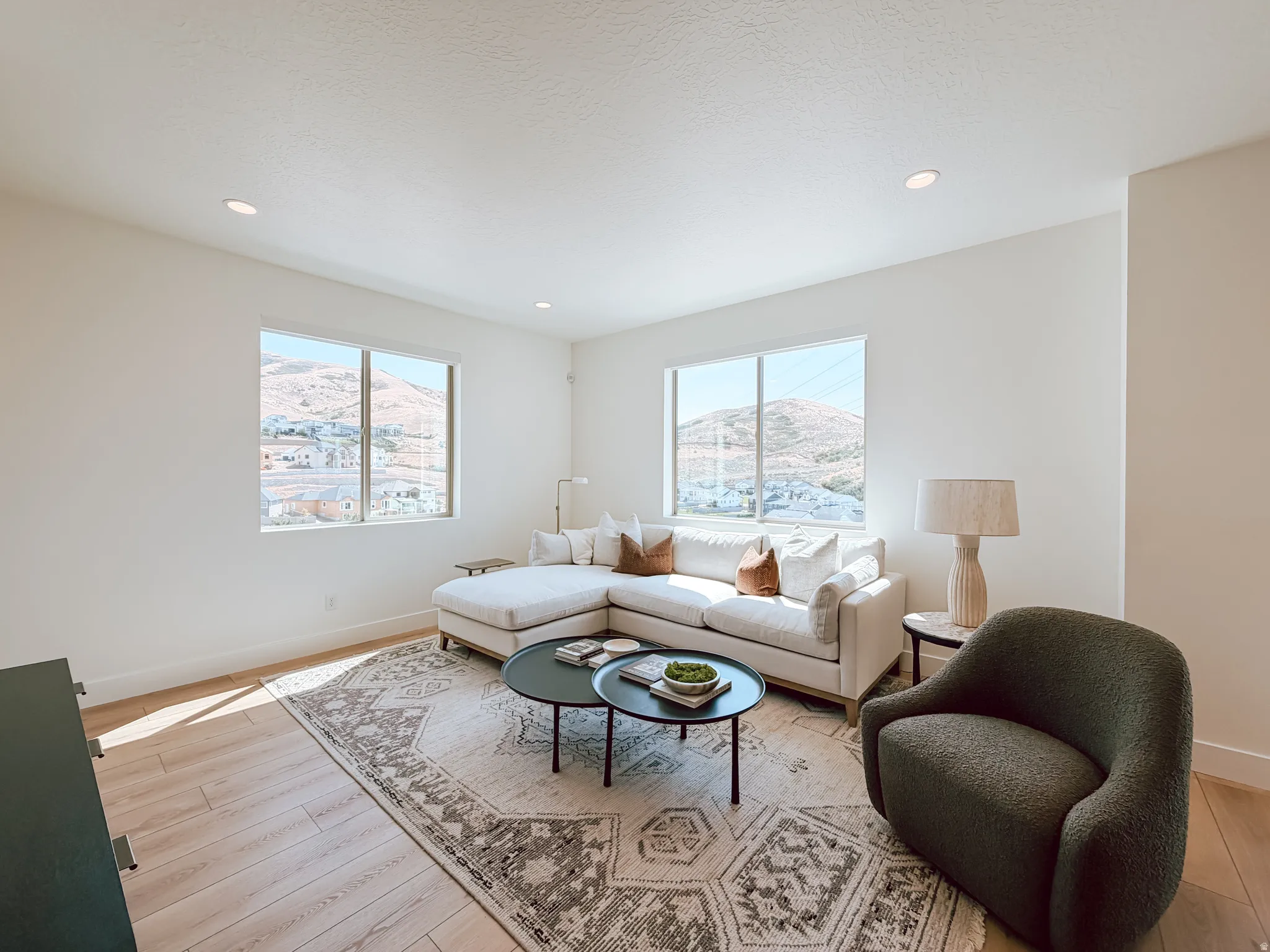 Bright living space with recessed lighting, large windows, wood-finish flooring, and white baseboards