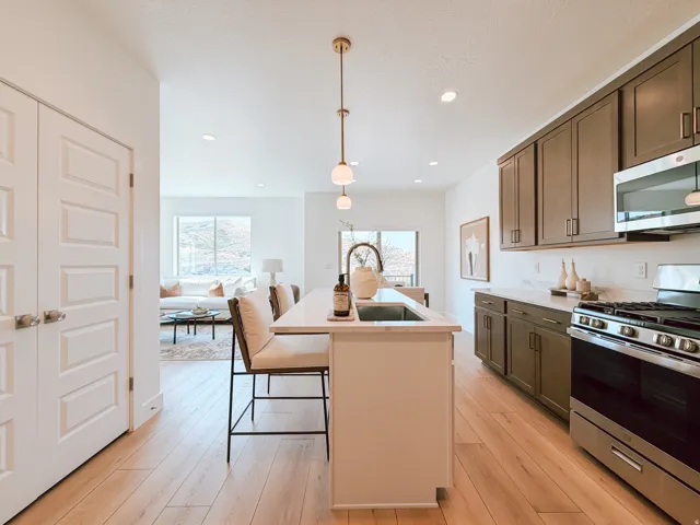 Modern kitchen featuring a central island with an integrated sink, light wood-finish flooring, dark cabinetry, stainless steel appliances, and recessed lighting