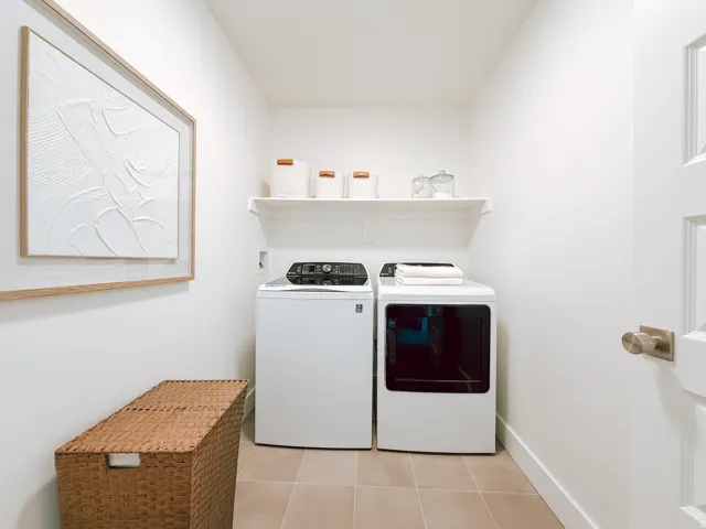 Laundry area featuring neutral tile flooring, a built-in wall shelf, and modern appliances