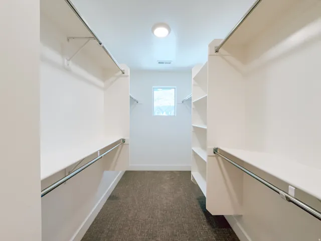 Spacious walk-in closet featuring white shelving units, multiple hanging rods, and recessed lighting
