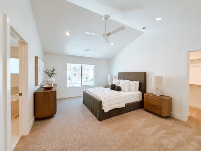 Vaulted ceiling featuring a ceiling fan and recessed lighting, plush patterned carpeting, a large window, and an open doorway revealing a walk-in closet