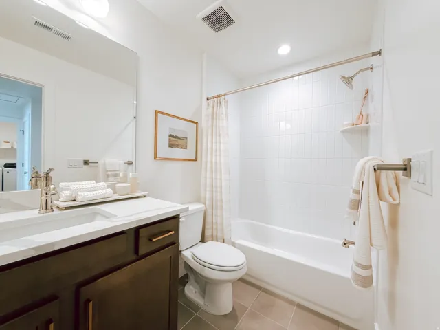 Bathroom featuring a dark wood-finish vanity with an integrated sink and light-toned countertop, a full-size mirror, a white tiled shower/tub combination, and gray tile flooring