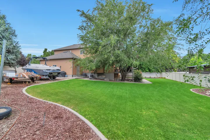 Expansive backyard featuring a lush lawn, mature trees, concrete curbing, and a stucco-clad exterior
