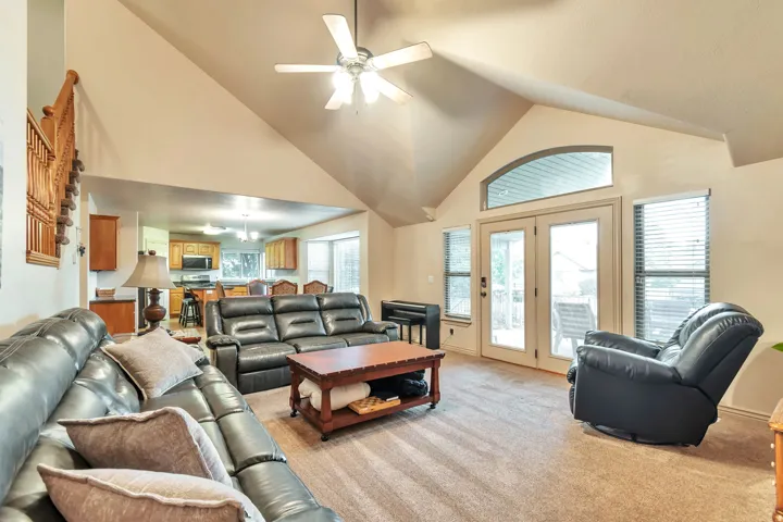 Carpeted living area featuring a vaulted ceiling and a ceiling fan with integrated lighting