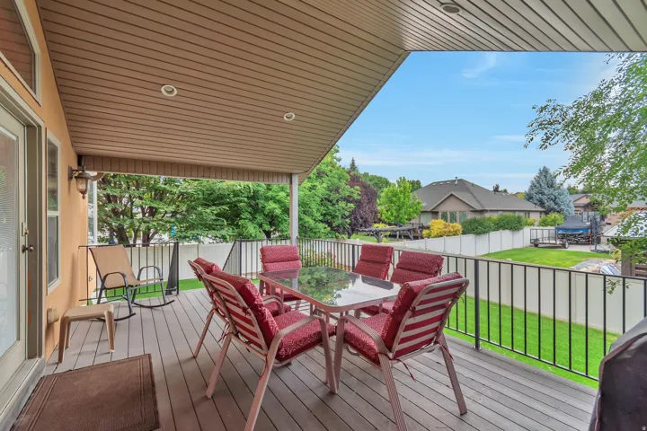Covered outdoor deck with composite wood-finish flooring, recessed lighting, and a black metal railing overlooking a green lawn