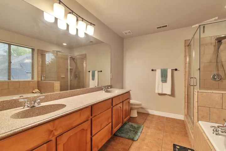 Bathroom featuring a long wood-finish vanity with dual sinks and a light-toned countertop