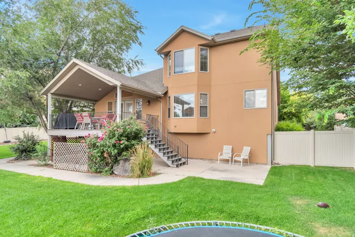 Spacious rear exterior featuring a covered deck, lower patio, mature trees, and a privacy fence