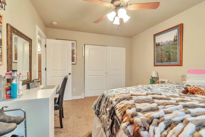Carpeted room featuring a ceiling fan with light kit, white bi-fold closet doors, a white arch-top interior door, and a built-in white desk with a framed mirror