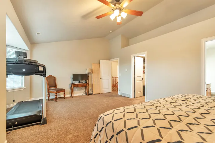 Carpeted room with a vaulted ceiling, a ceiling fan with light fixture, and multiple doorways