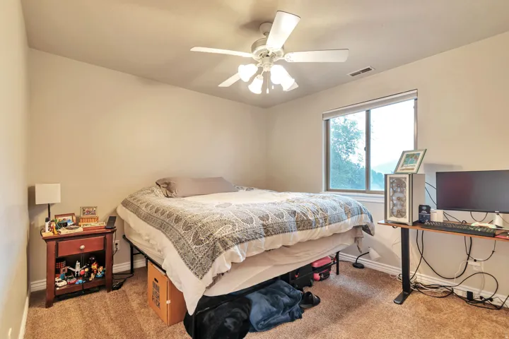 Carpeted room featuring a window with a natural backdrop, a ceiling fan with integrated lighting, and neutral wall tones