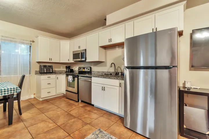 Kitchen featuring white cabinetry, granite-style countertops, stainless steel appliances, and large format tile flooring