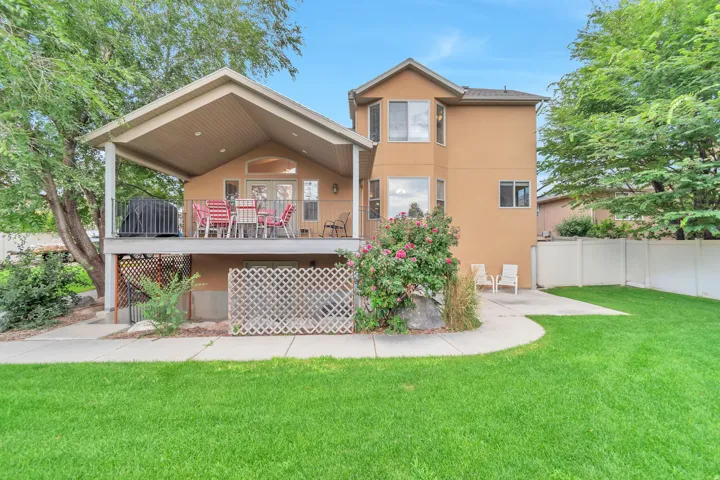 Rear exterior featuring an elevated covered deck with a pitched roof, a lower-level patio, and a manicured lawn