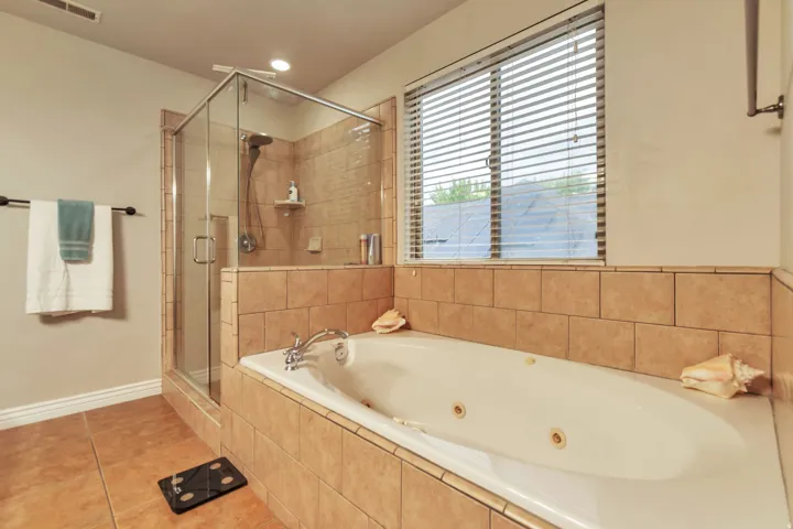 Tiled bathroom featuring an enclosed shower with glass walls, a jetted soaking tub, a built-in tiled tub surround, and a window with horizontal blinds