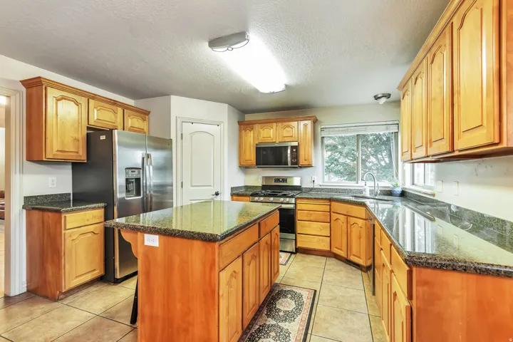 Kitchen featuring a center island, wood cabinetry, stone countertops, stainless steel appliances, and tile flooring