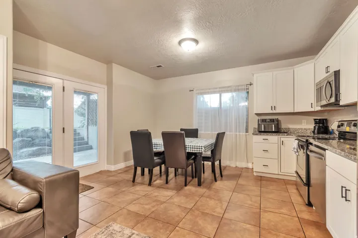 Kitchen and dining area featuring white cabinetry, stainless steel appliances, granite countertops, and tile flooring