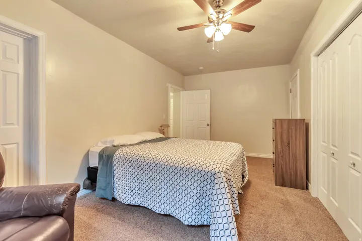 Carpeted room featuring a ceiling fan with light fixture, three paneled doors, and neutral wall tones