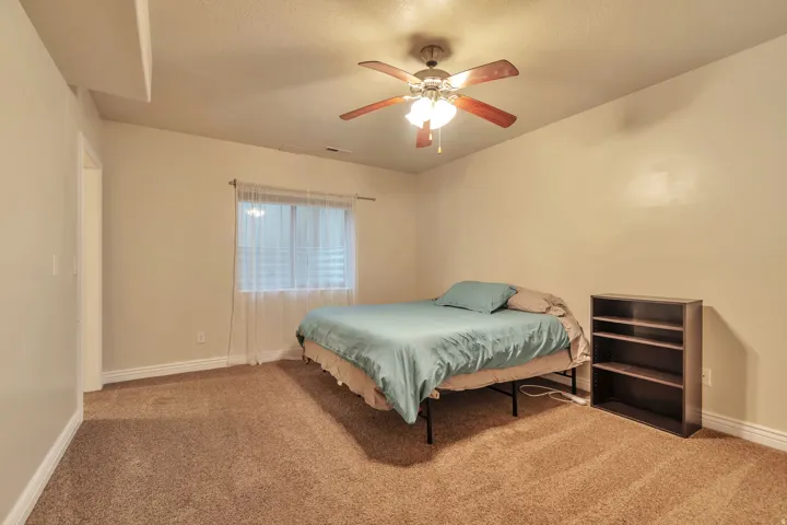 Carpeted room featuring a ceiling fan with integrated lighting, a window with blinds and sheer curtains, and light-toned walls with white baseboards