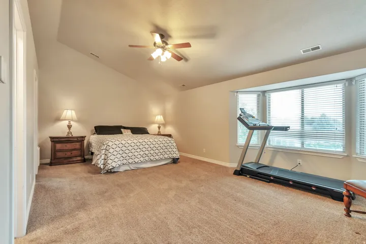 Carpeted room featuring a bay window, sloped ceilings, and a ceiling fan with integrated lighting