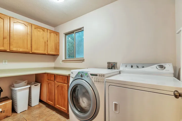 Laundry room featuring wood-finish cabinetry, a light-toned countertop, and tile flooring