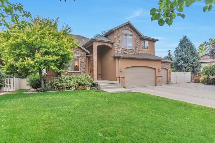 Stucco and stone facade home featuring a two-car garage, arched entry, and mature landscaping