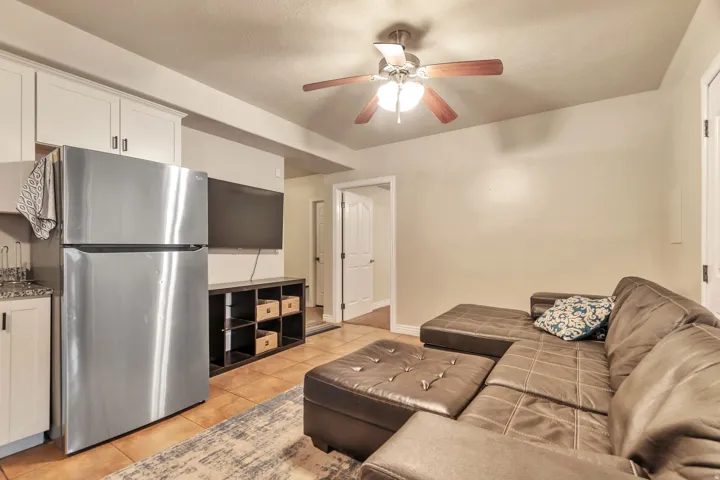 Compact living area featuring durable tile flooring, a functional kitchenette with white cabinetry, a stainless steel refrigerator, and a ceiling fan with integrated lighting