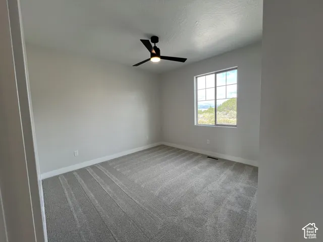 Neutral-toned interior featuring wall-to-wall carpeting, a multi-pane sliding window, and a matte black ceiling fan with an integrated light fixture