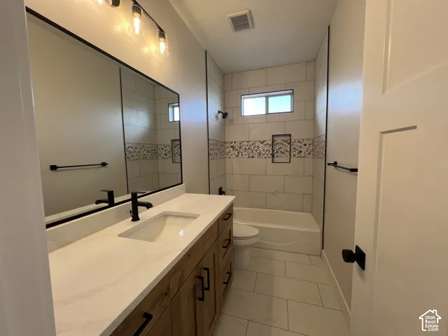 Bathroom featuring a vanity with a white countertop and undermount sink, matte black hardware, a large framed mirror, and a tub-shower combination with decorative tile inlay and built-in shelving