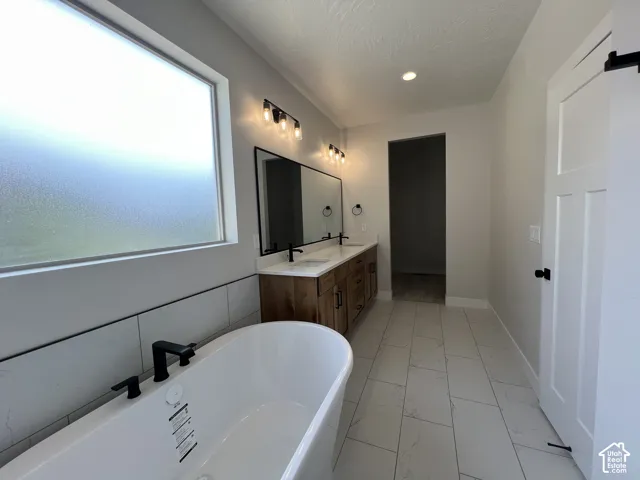 Freestanding soaking tub with matte black fixtures, dual-sink wood-finish vanity, large framed vanity mirror, and rectangular tiled flooring
