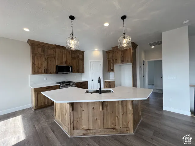 Kitchen featuring a custom-shaped center island with a stone-surface countertop, wood-finish cabinetry, recessed lighting, and pendant fixtures
