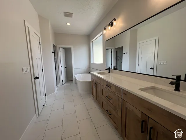 Dual-sink vanity with wood-finish cabinetry, quartz countertops, matte black fixtures, full-width mirror, and a freestanding soaking tub