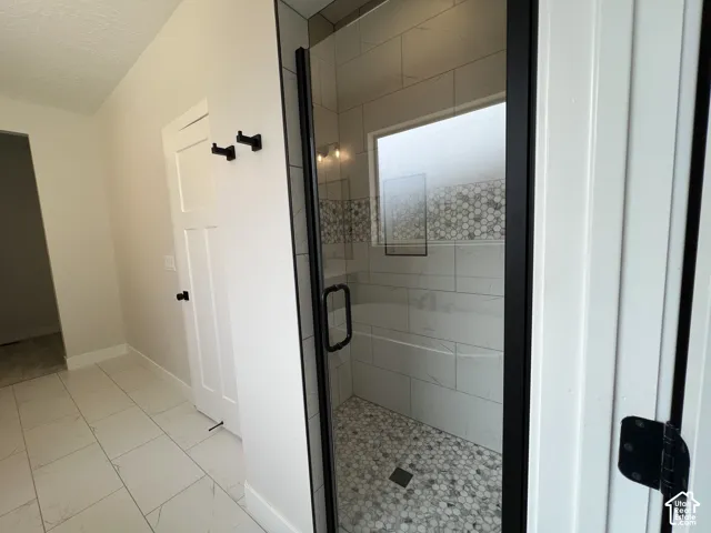 Walk-in shower featuring matte black fixtures, glass enclosure, rectangular wall tile, and patterned stone floor tile