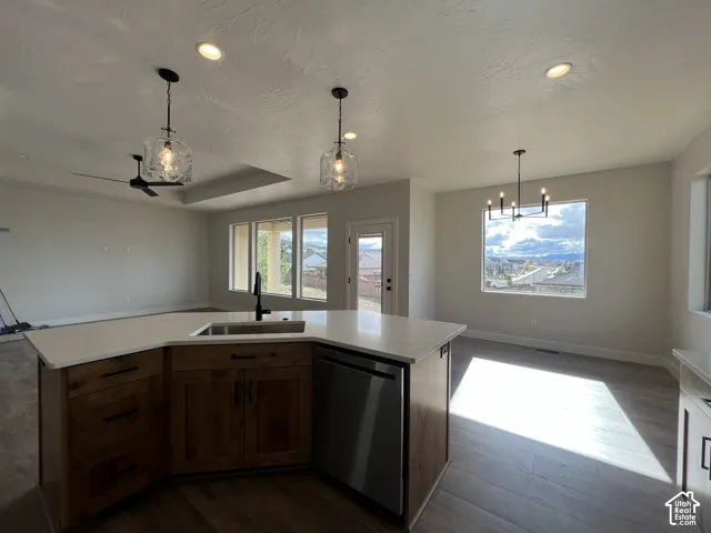 Kitchen island featuring a stone-surface countertop, an undermount sink with a dark-finish faucet, wood-finish cabinetry, recessed lighting, and pendant fixtures