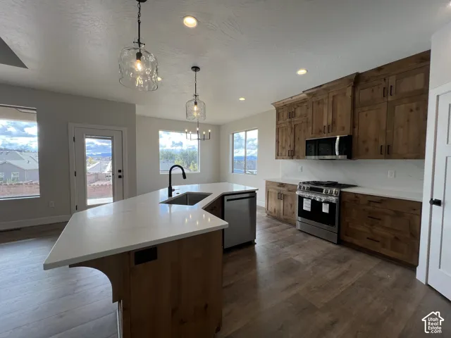 Kitchen featuring stained wood cabinetry, quartz countertops, a central island with an undermount sink, stainless steel appliances, and wood-finish flooring