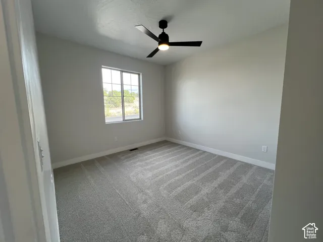 Neutral-toned interior space featuring light-colored wall paint, plush carpeting, a multi-pane grid window, and a matte black ceiling fan with integrated lighting