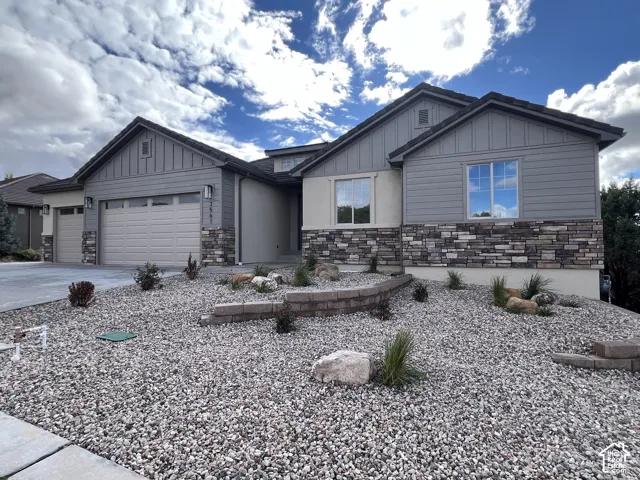 Single-story residence featuring a multi-material exterior of horizontal lap siding, vertical board-and-batten siding, and stone veneer accents, complete with a multi-car garage and landscaped xeriscaping with stone retaining walls