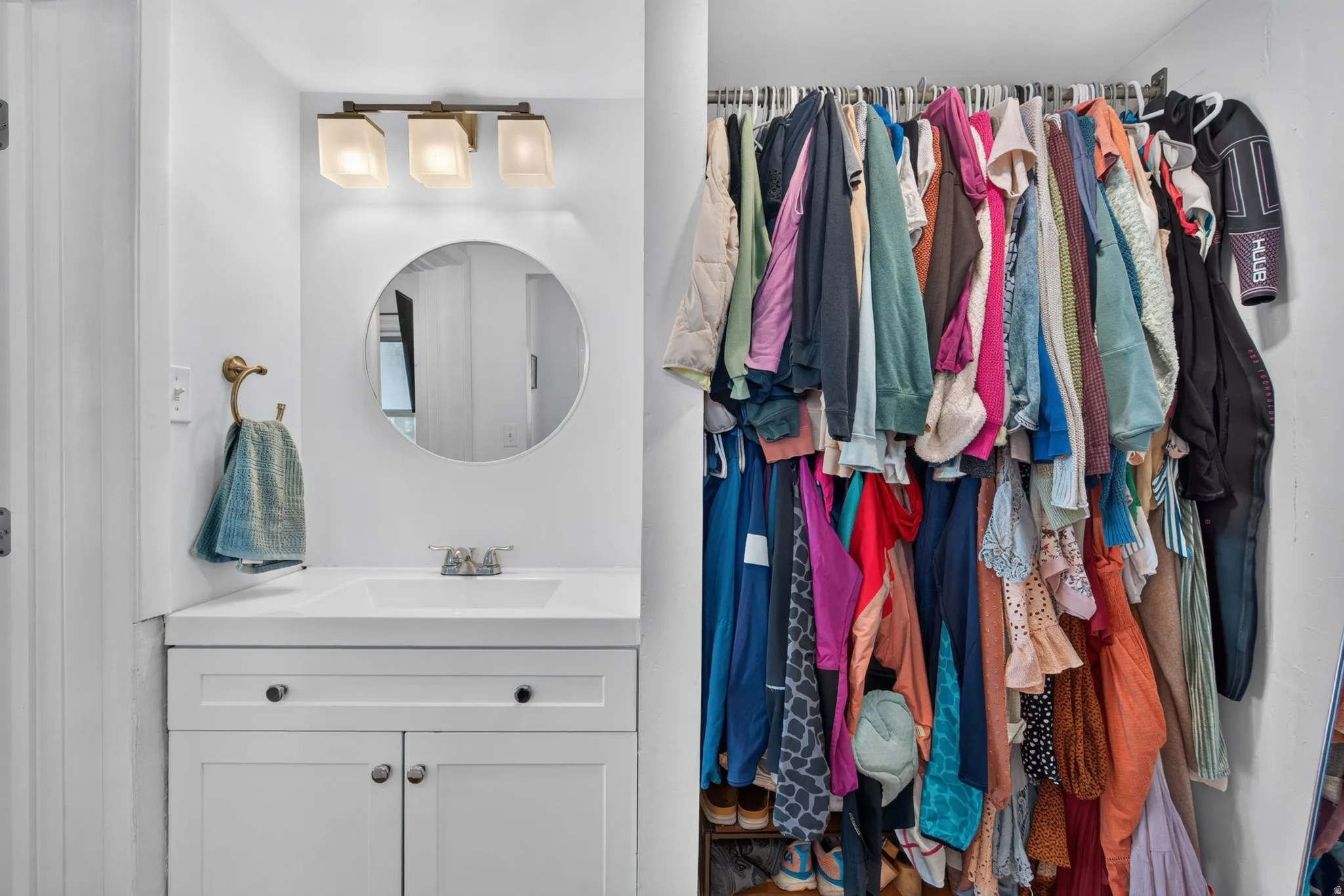 White vanity with an integrated sink and brushed nickel hardware, complemented by a circular mirror and a three-light fixture with frosted glass shades