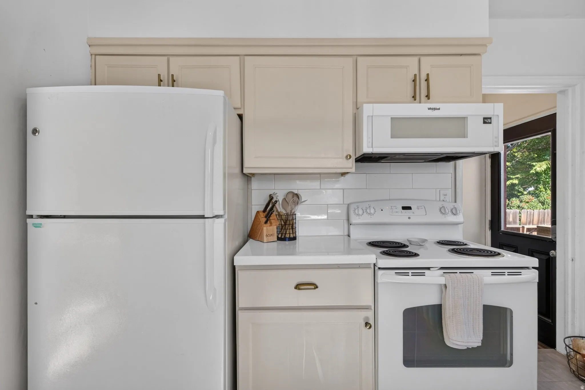 Kitchen featuring white appliances, upper and lower cabinetry, white subway tile backsplash, and light-toned countertops