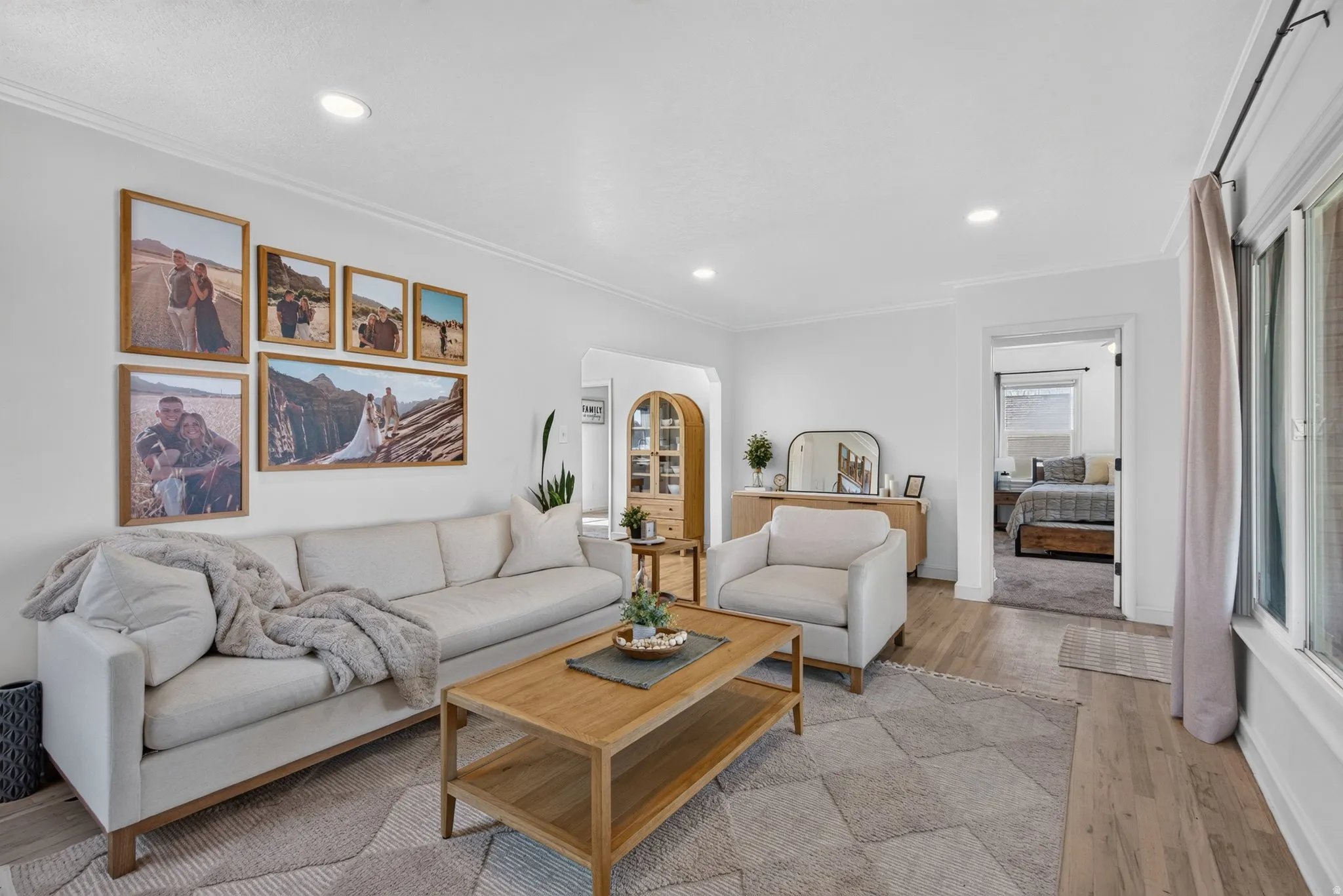 Spacious living area featuring light wood-finish flooring, white walls, recessed lighting, and crown molding