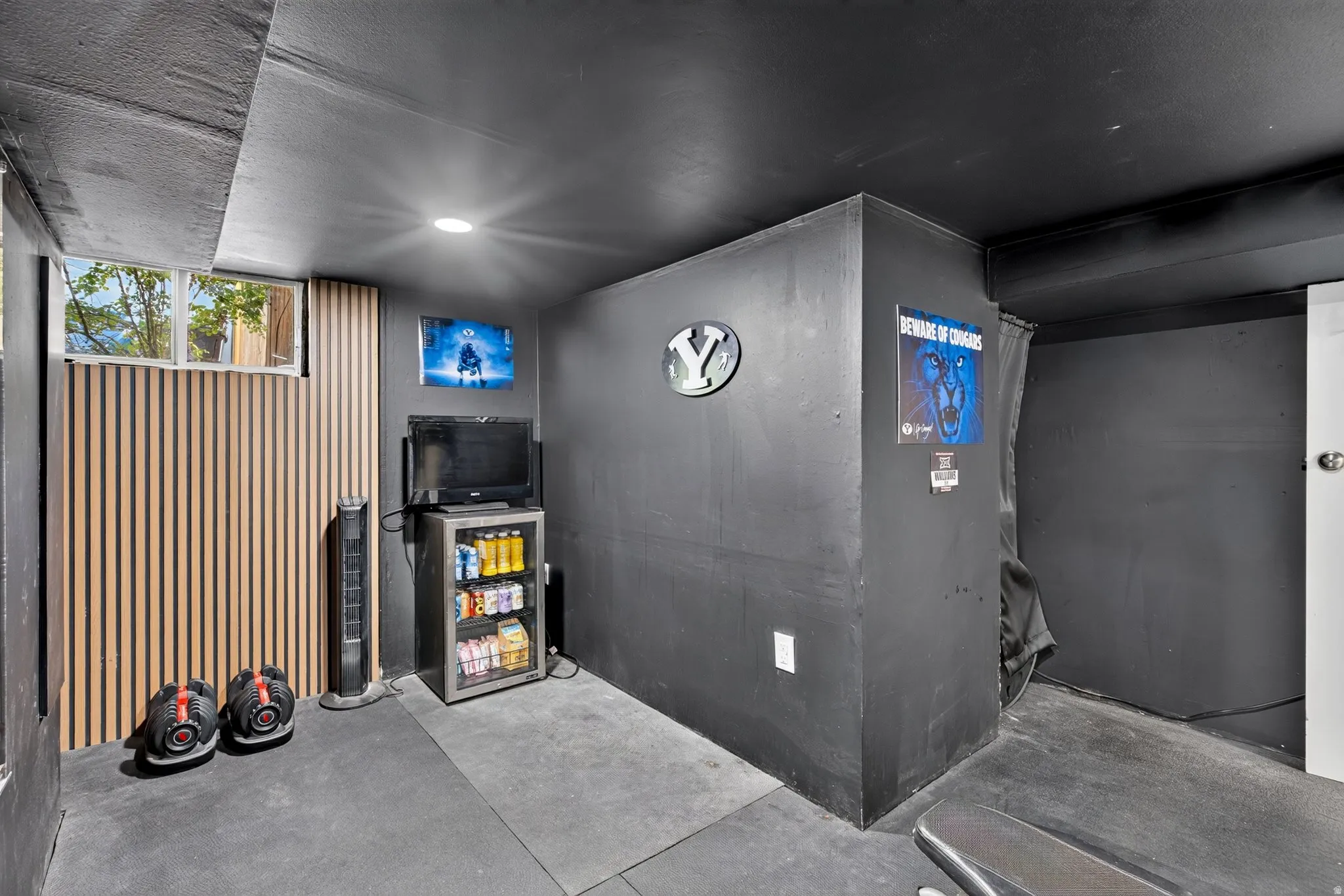 Recessed lighting illuminates a space featuring dark-toned walls and ceiling, a window, and wood-finish paneling