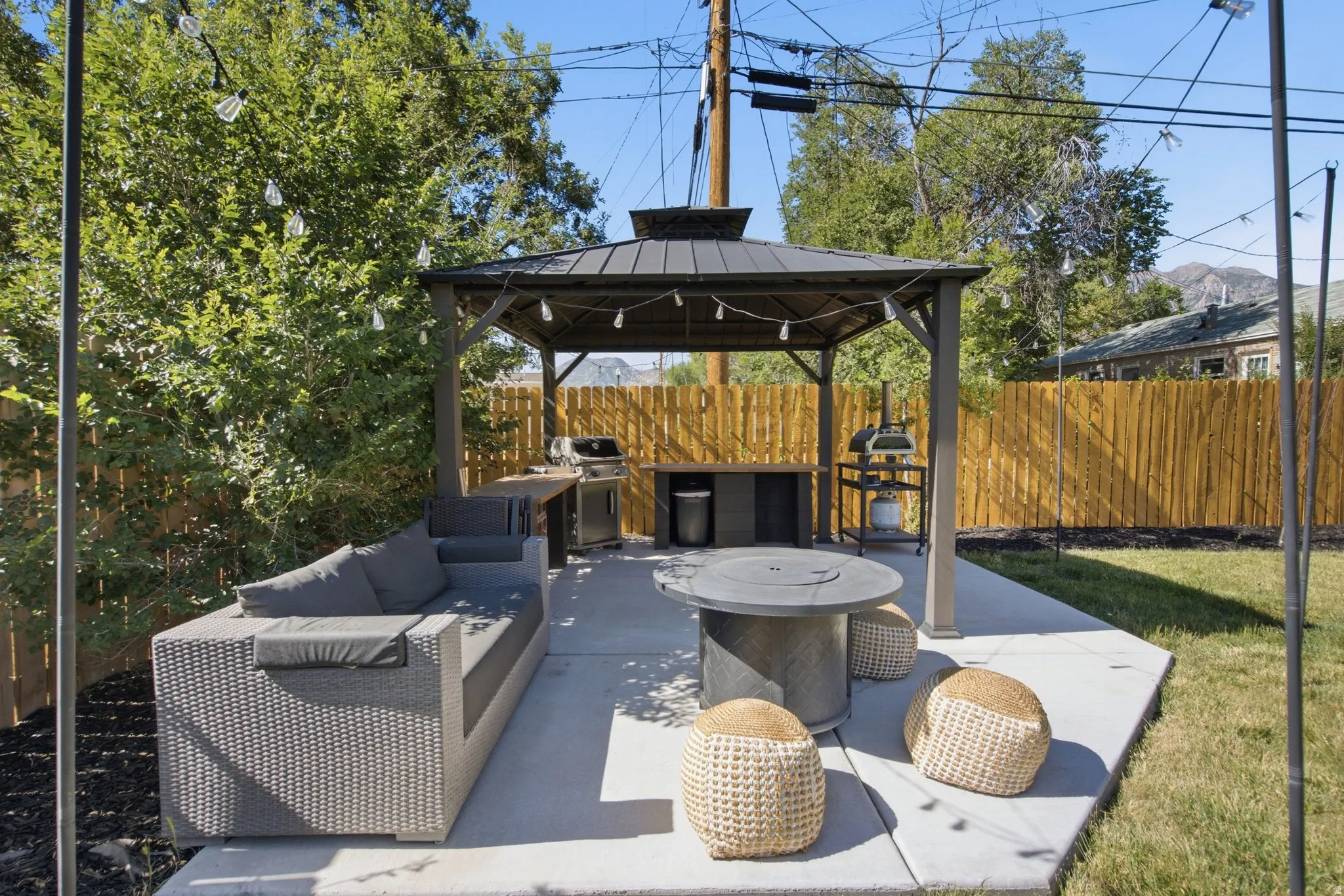 Expansive concrete patio featuring a shaded gazebo with string lights, integrated counter space, and a built-in fire pit
