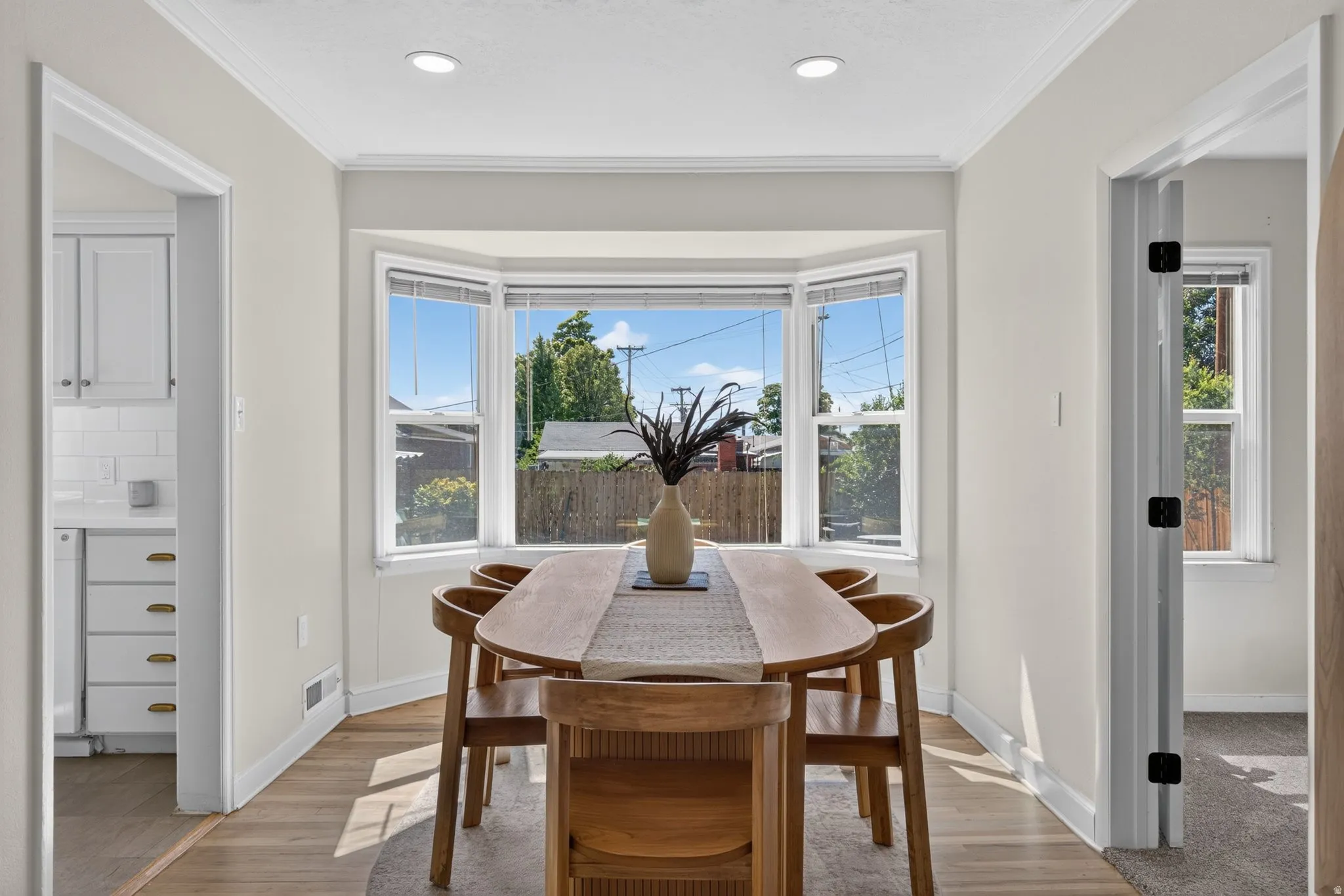 Bay window with natural light, recessed lighting, crown molding, wood-finish flooring, and light-colored walls