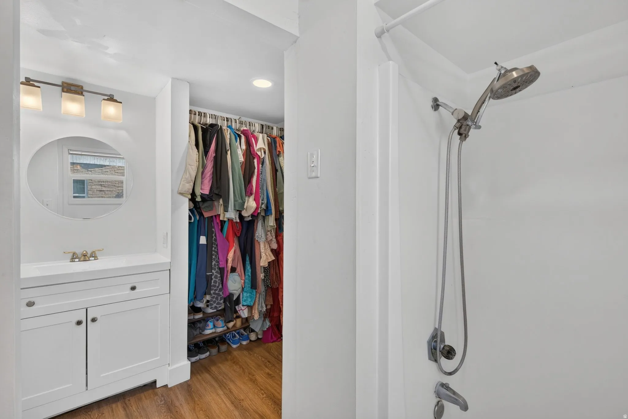 White bathroom vanity with circular mirror, overhead vanity lighting, and integrated sink