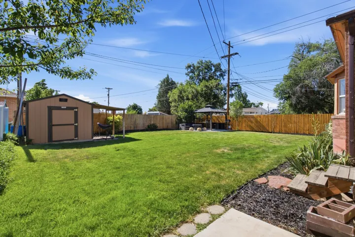 Expansive backyard featuring a manicured lawn, full perimeter wood fencing, and a detached storage shed with an attached covered patio