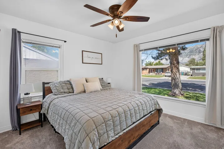 Spacious room featuring carpeting, a multi-pane window with mountain scenery, an additional window with white blinds, a ceiling fan with integrated lighting, and white baseboards