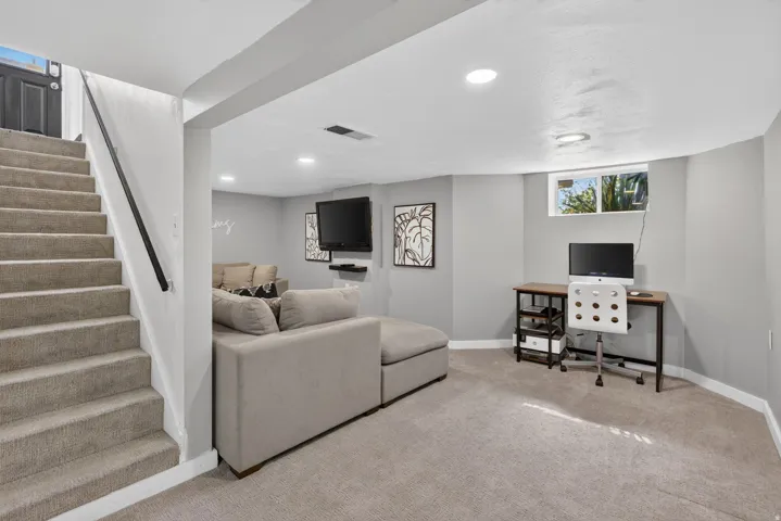 Carpeted staircase with a black handrail providing access to a lower level with recessed lighting, a built-in window, and light gray wall finishes