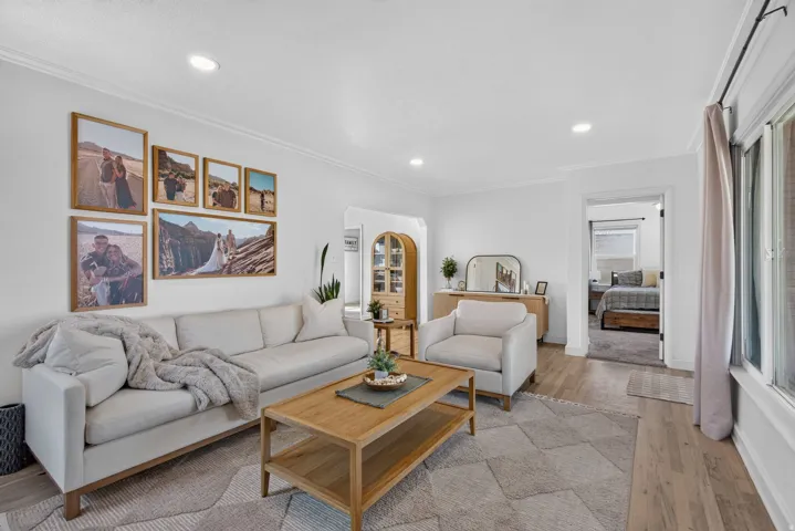 Spacious living area featuring light wood-finish flooring, white walls, recessed lighting, and crown molding