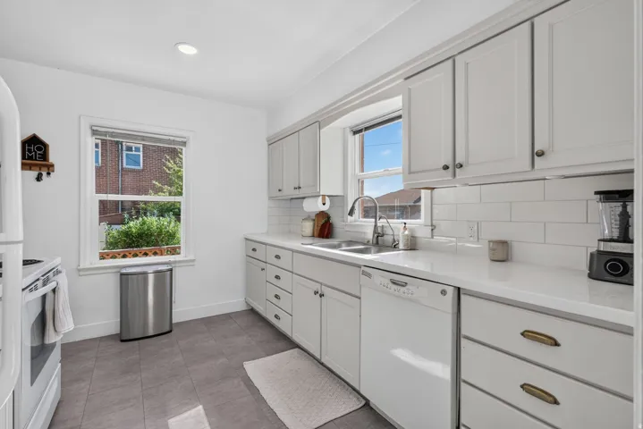 Bright kitchen featuring white shaker-style cabinetry, white subway tile backsplash, and light-toned countertops