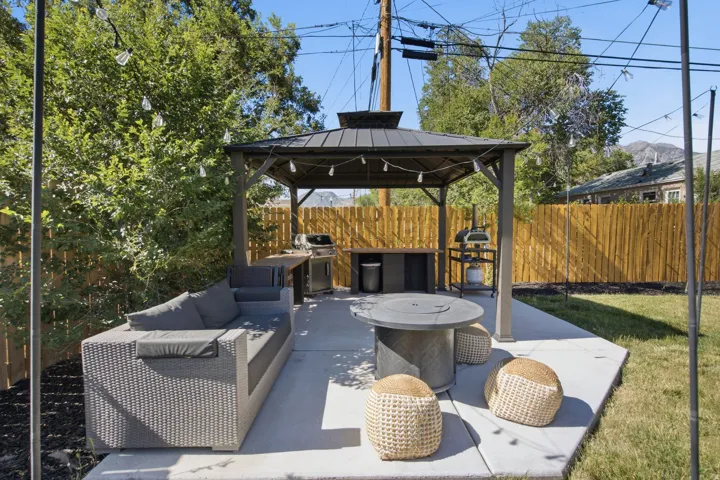 Expansive concrete patio featuring a shaded gazebo with string lights, integrated counter space, and a built-in fire pit