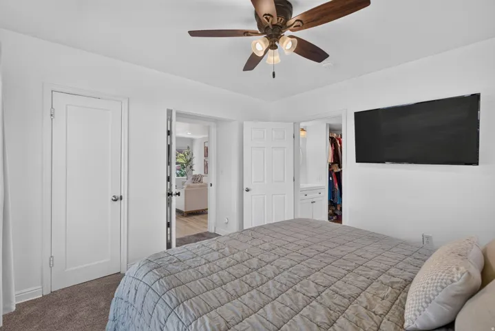 Bedroom featuring a ceiling fan, wall-mounted display, and carpeted flooring