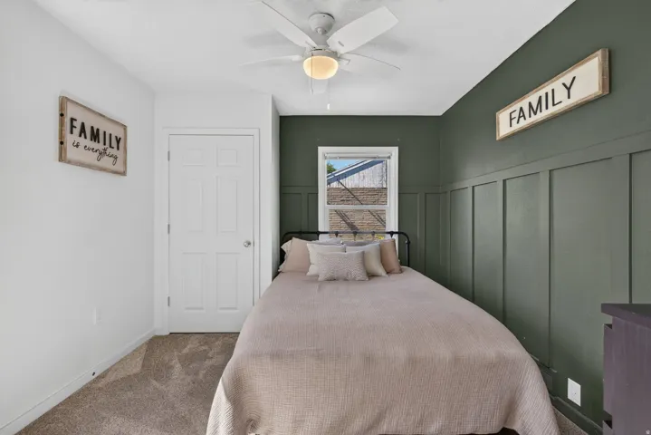 Carpeted room featuring a ceiling fan with integrated lighting, a four-panel interior door, and a window with white trim